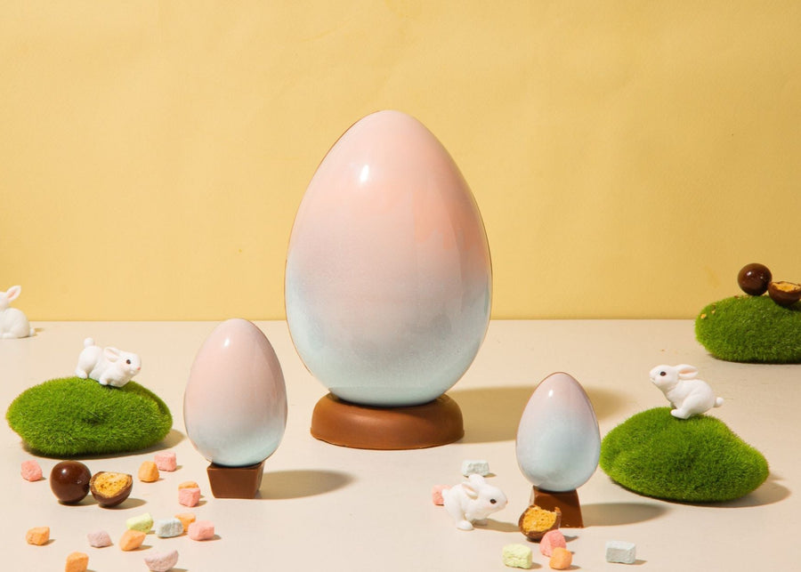 Milk chocolate easter eggs in baby pink and baby blue with mini rainbow marshmallows and little bunny figurines all around